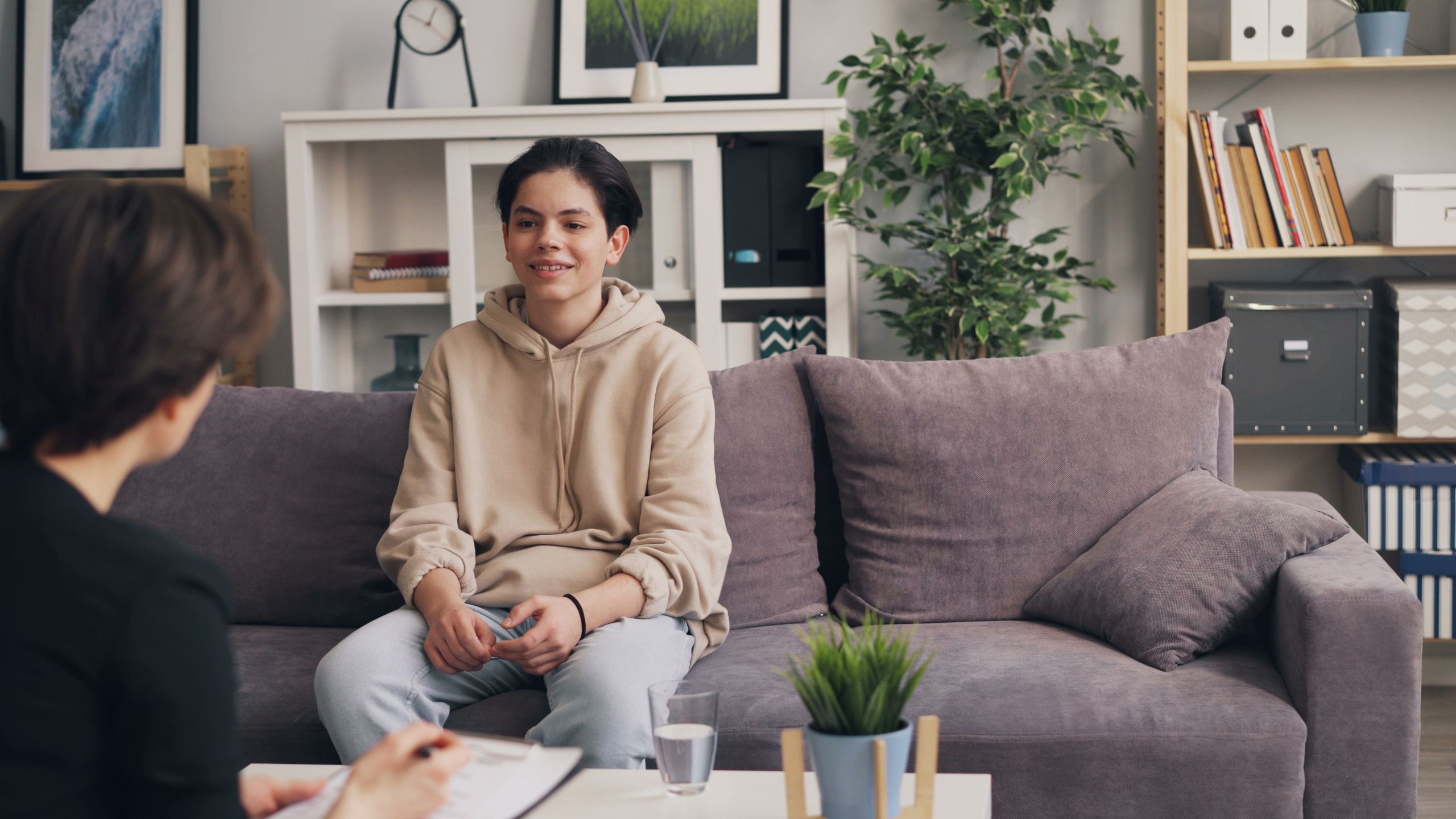 A teenager in a therapy session discussing with a professional in a modern, comfortable setting.
