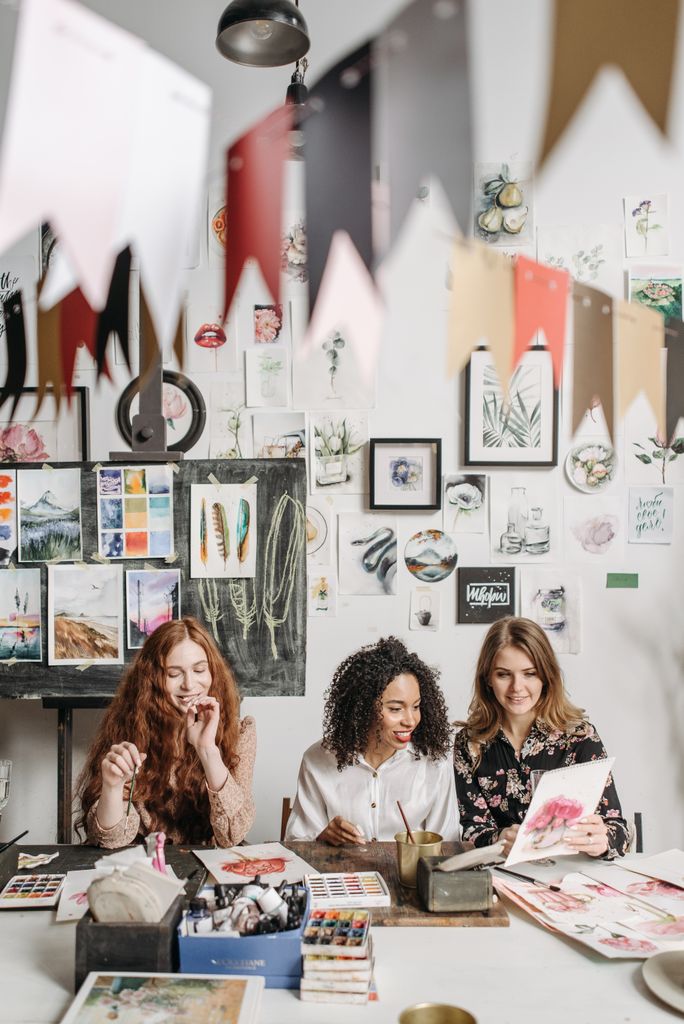 Three women enjoy a painting session in a colorful, decorated art studio, filled with creativity and laughter.